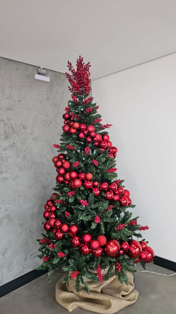 Green artificial christmas tree with spiral red christmas balls and a burlap at the base